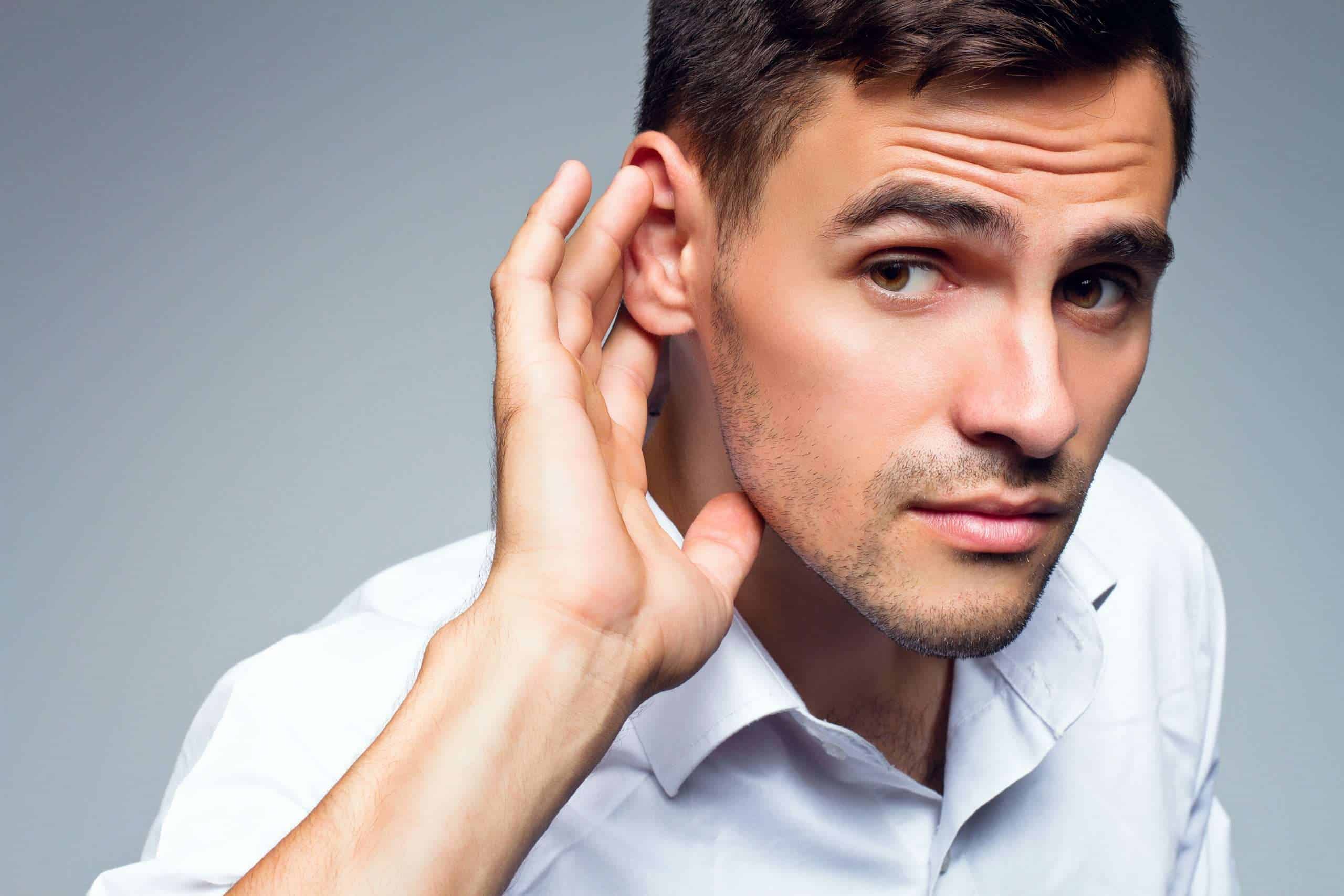 Young businessman holds his hand near ear.