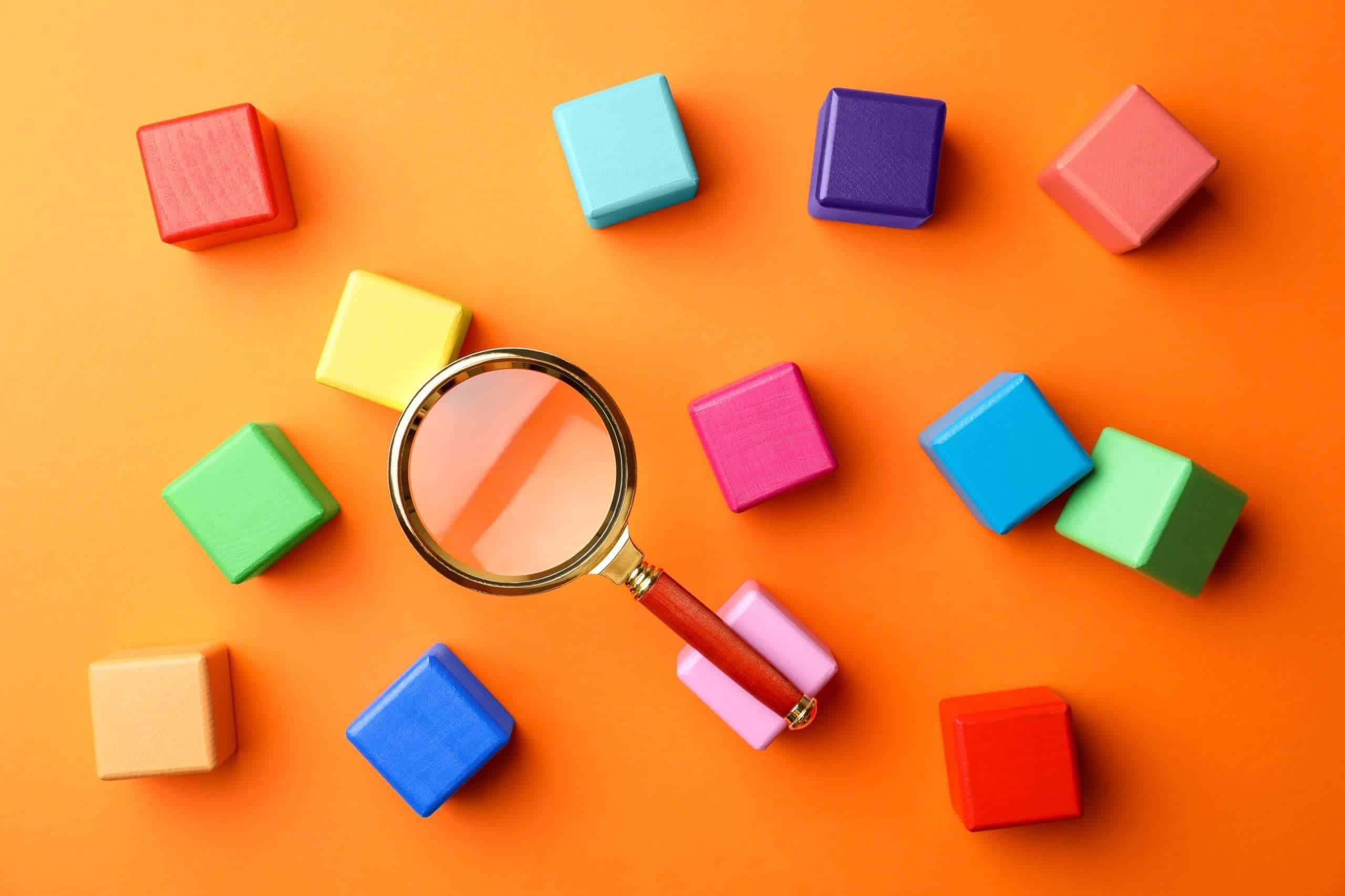 Different colorful cubes and magnifier glass on orange backgroun