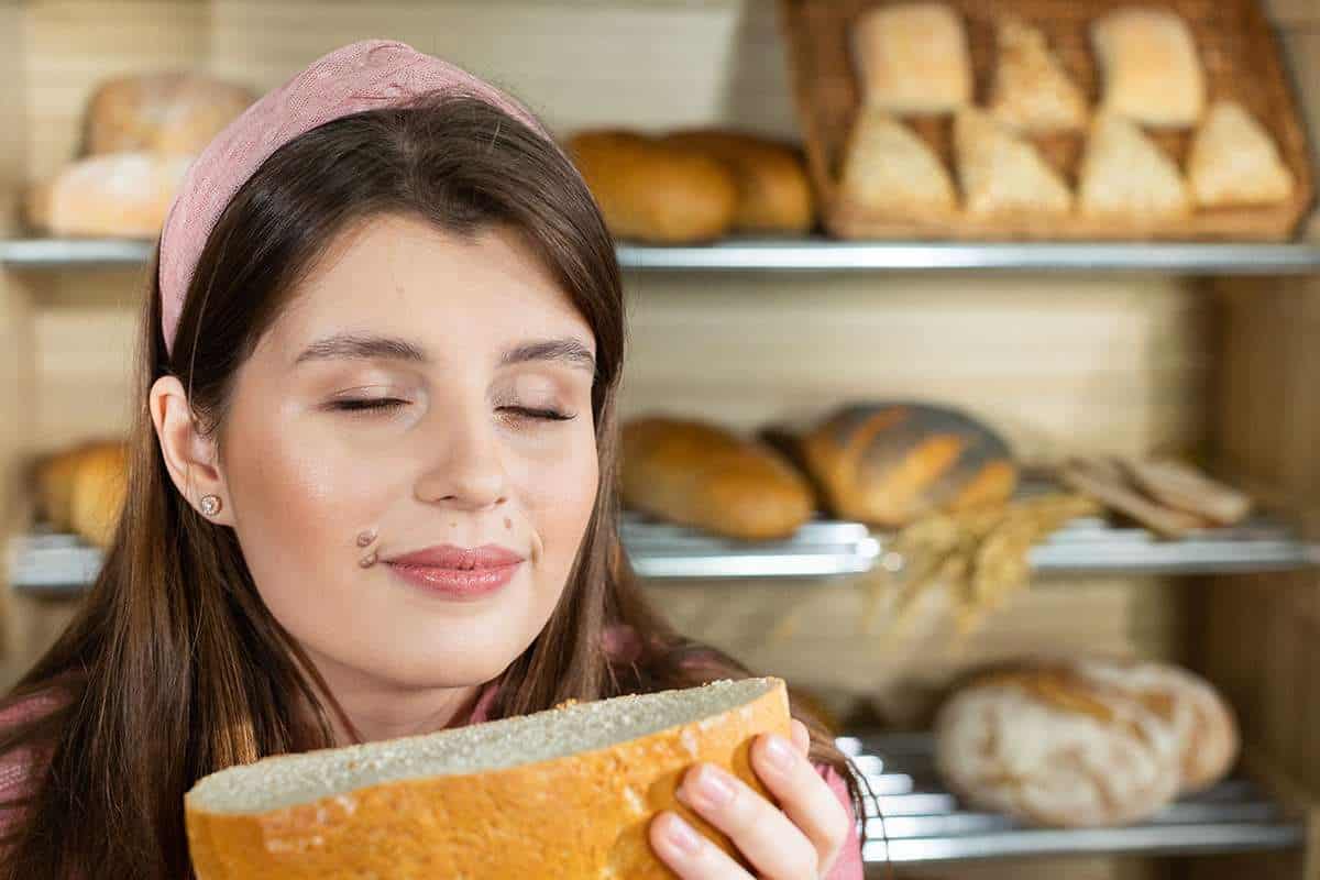 The frame is very close. After cutting a round wheat loaf of bread, an attractive saleswoman raves about the aroma while smelling its delightful aroma.