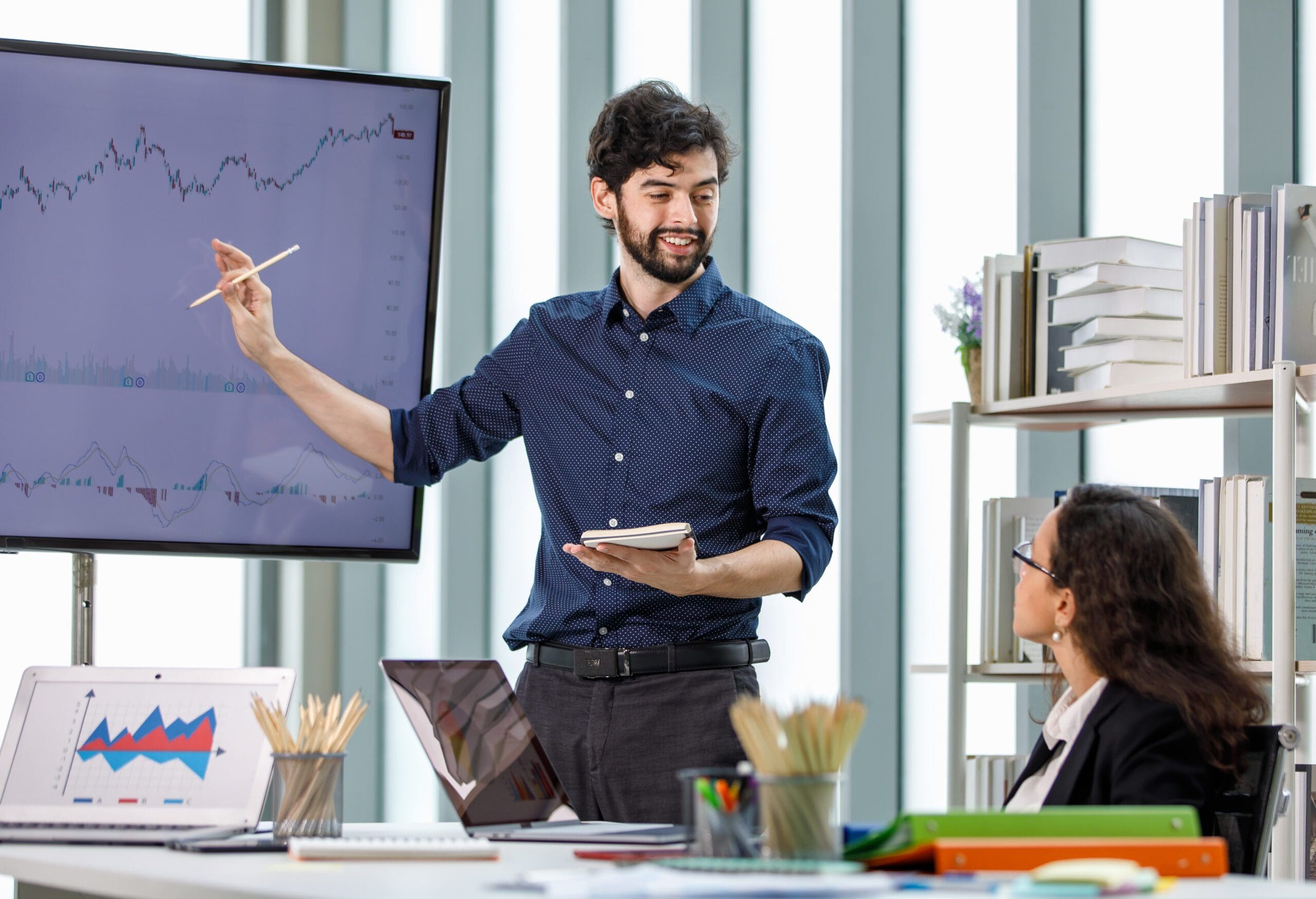 Hispanic bearded male businessman trainer teaching coaching new recruitment African American female businesswoman employee in formal suit sitting studying learning company graph chart strategy