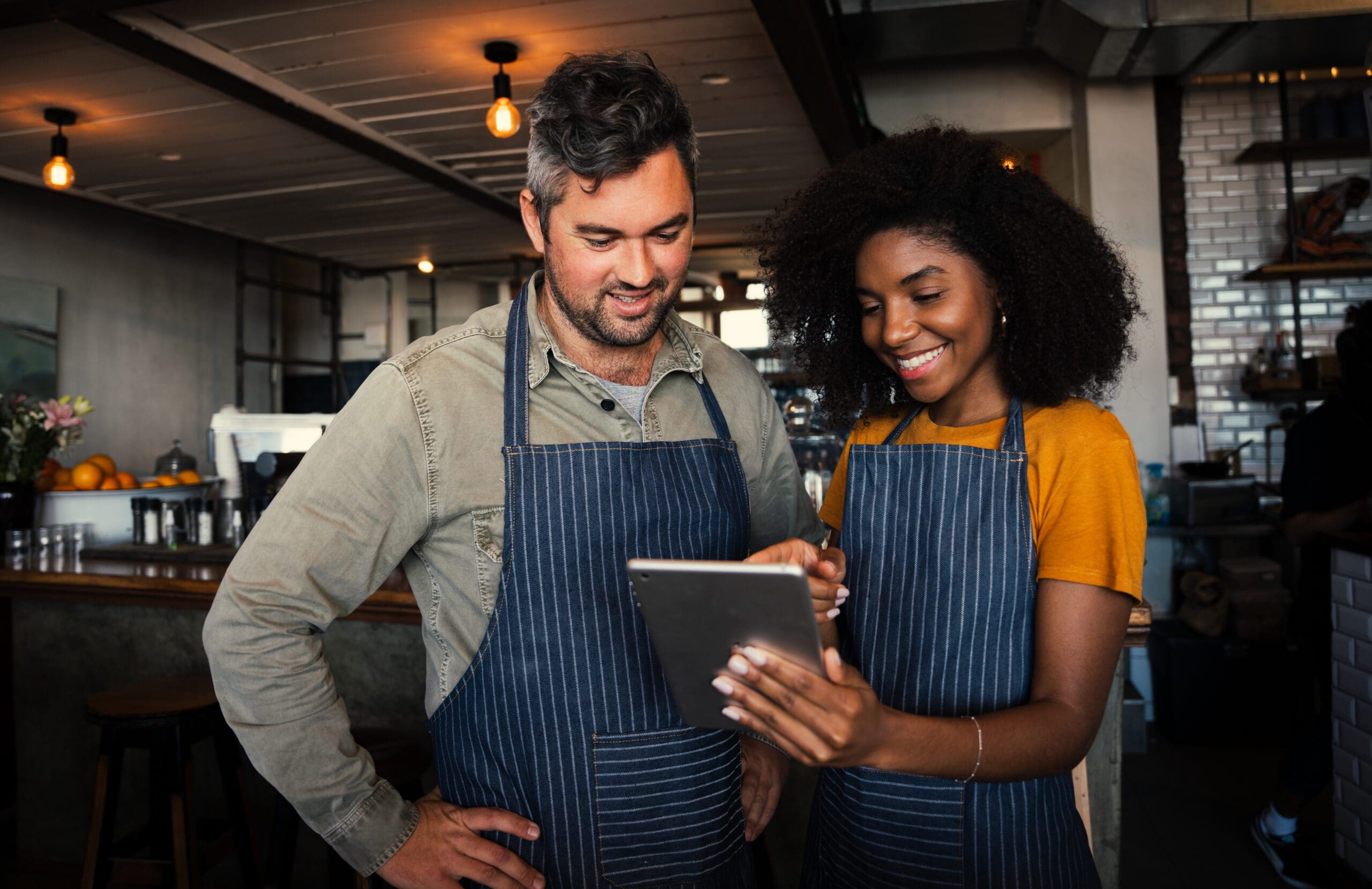 Male and female coffee shop owners smiling at tablet in coffee shop.