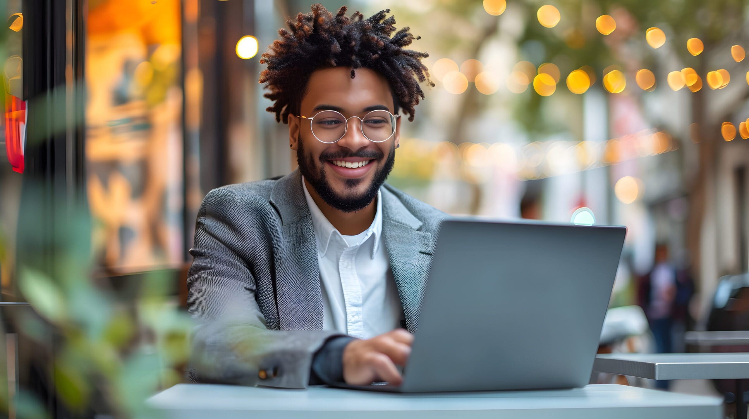 A contented young Latino businessman sitting outside with a laptop. A happy Hispanic man studying or working in a city café, using a computer to do e-learning or hybrid work, and looking for a job onl