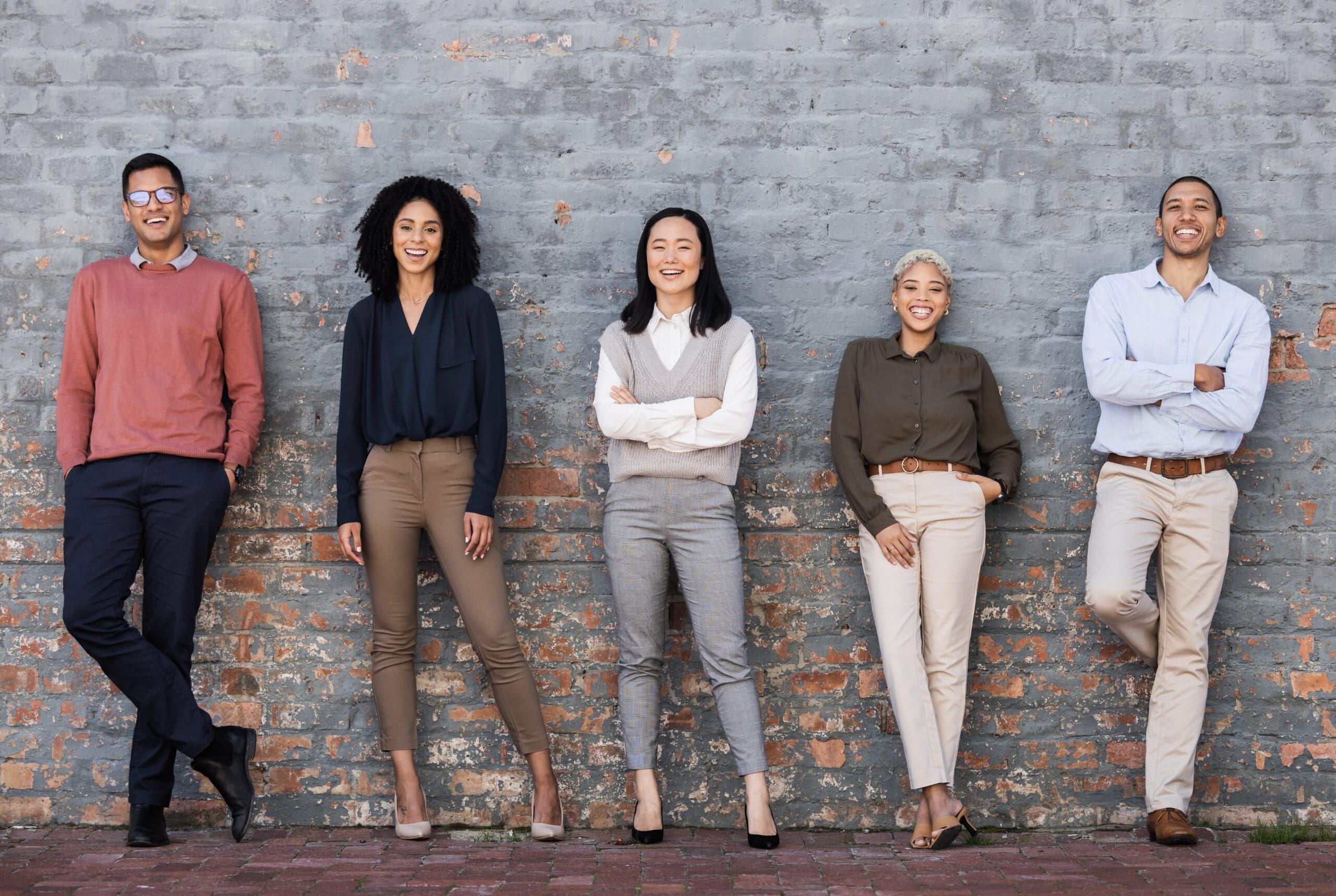 Portrait, collaboration and goals with a business team standing together, leaning on a brick wall. Teamwork, mindset and vision with a man and woman employee group outside for future success